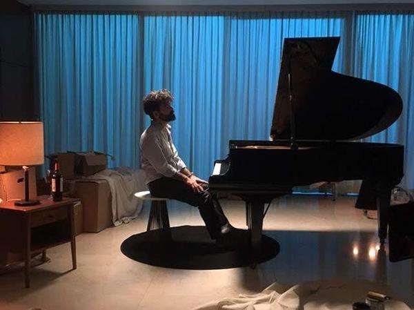 Antonio sentado frente a un piano de cola, con cortinas azules